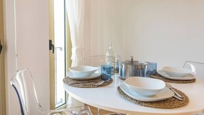 A dining table set with white bowls, plates, and cutlery, accompanied by a metal pot and glass pitcher, with woven placemats.