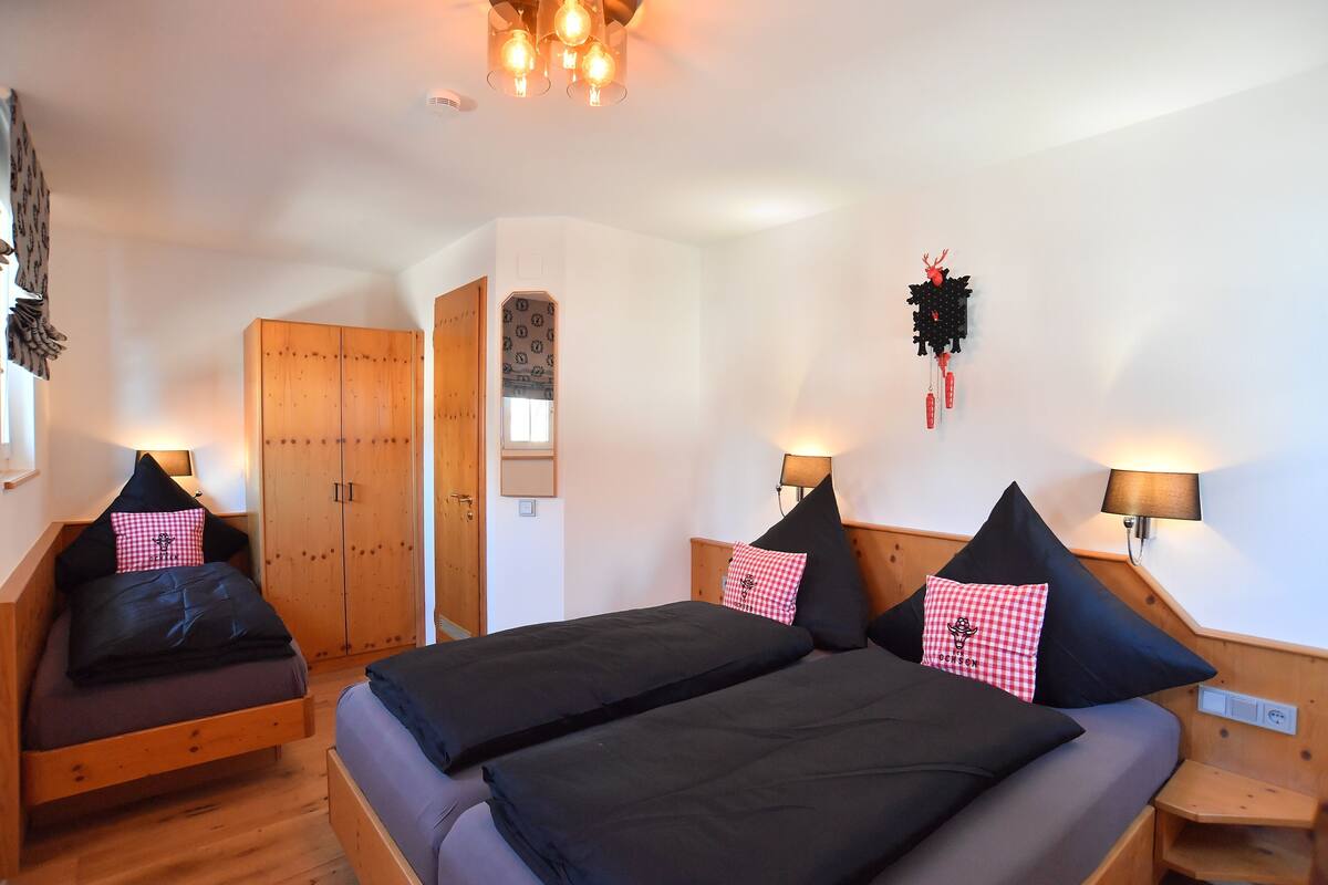 A room with two beds, wooden wardrobe, and wall-mounted lamps.