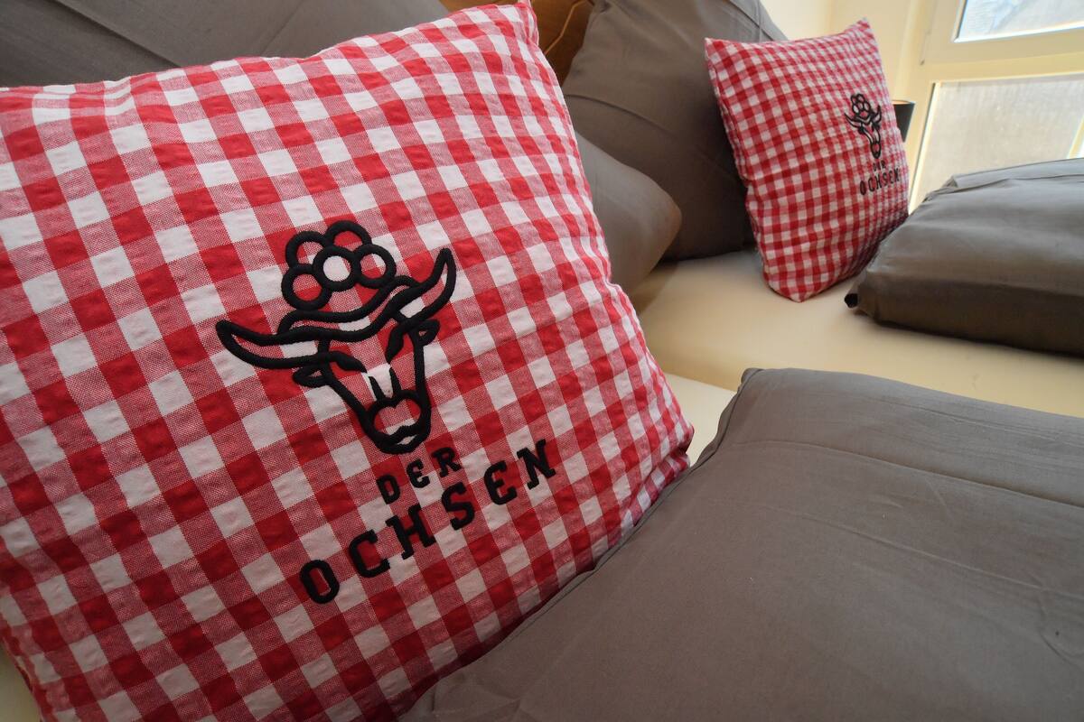 A sofa with red and white checkered pillows and a brown cushion.
