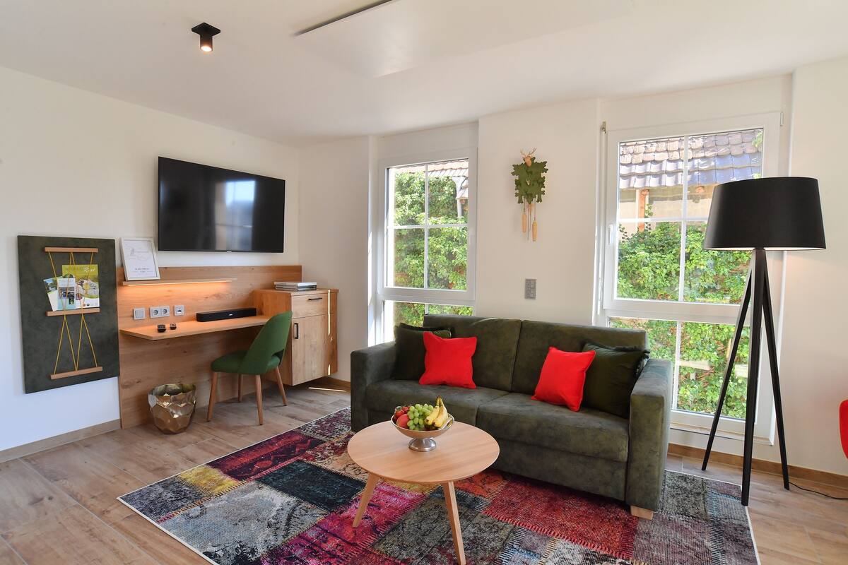 A modern living room with a sofa, a desk, a TV, and a large window.