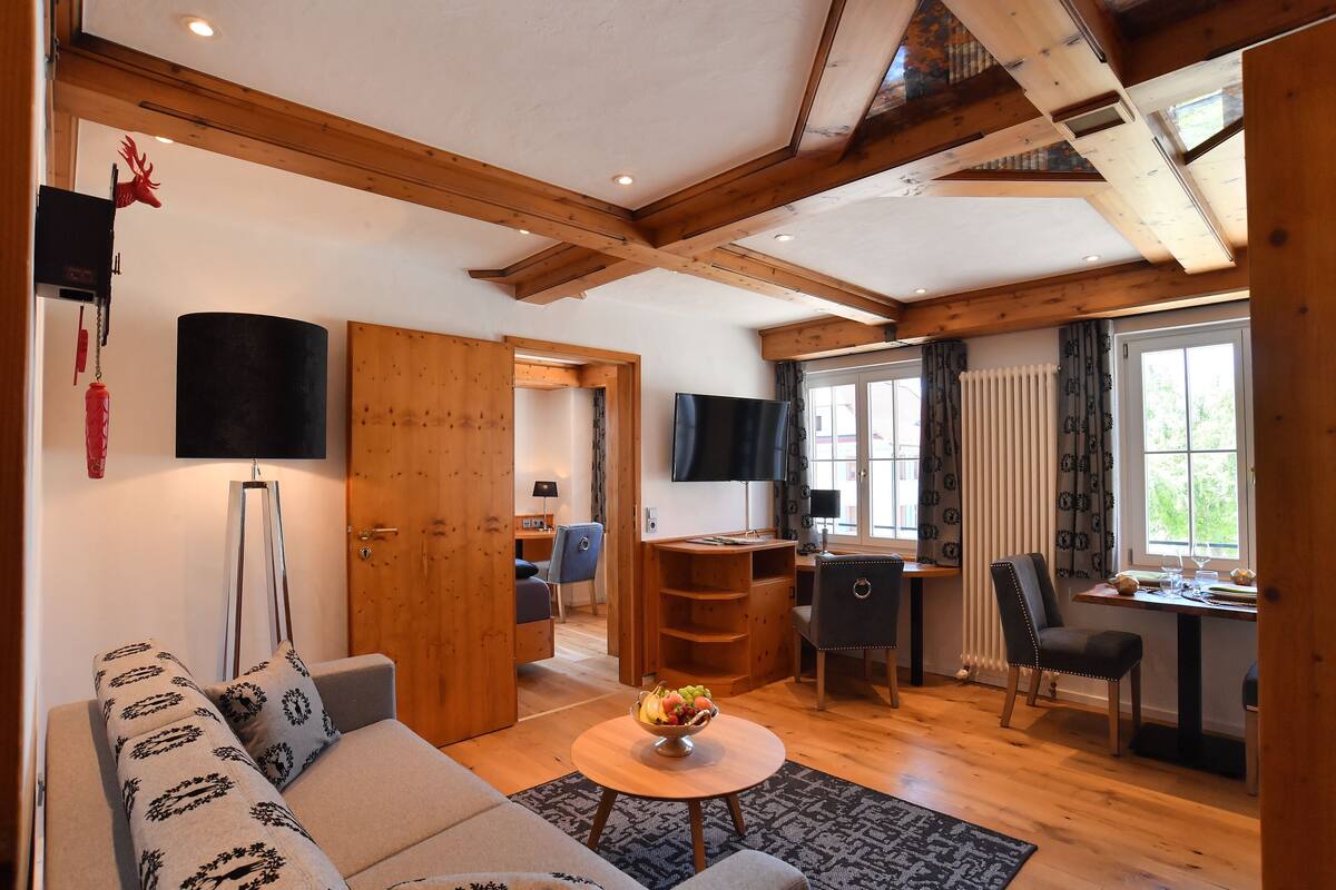 A cozy living room with a sofa, a coffee table with fruit, a TV, and a dining area with chairs and a table.