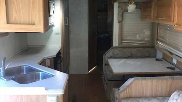 Een compact camperinterieur met een kitchenette, een eethoek en een slaapgedeelte.