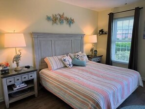 A bedroom with a bed, two nightstands, a window with curtains, and wall decor.