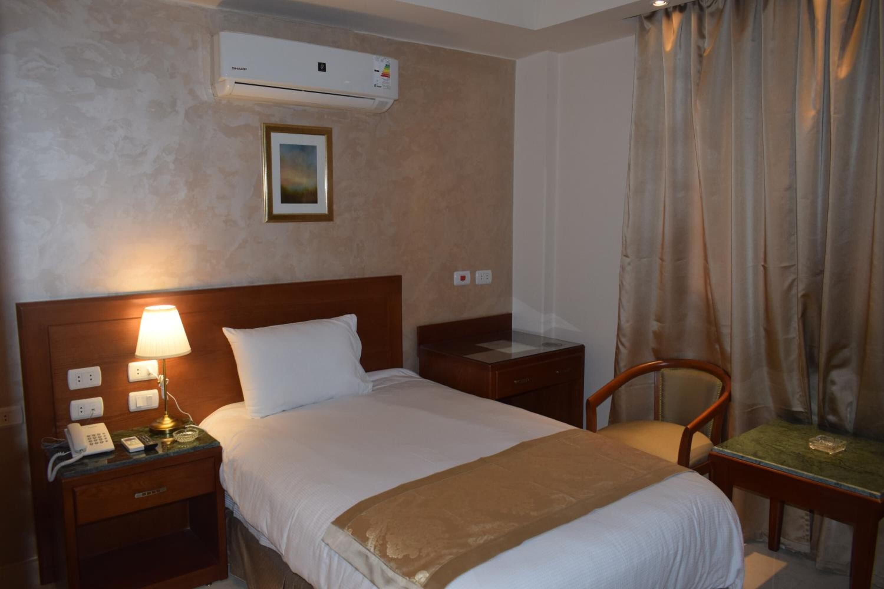A hotel room with a bed, bedside lamp, nightstand, phone, and an air conditioning unit.