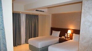 Een hotelkamer met twee bedden, een nachtkastje met een lamp en een airconditioningunit aan het plafond.