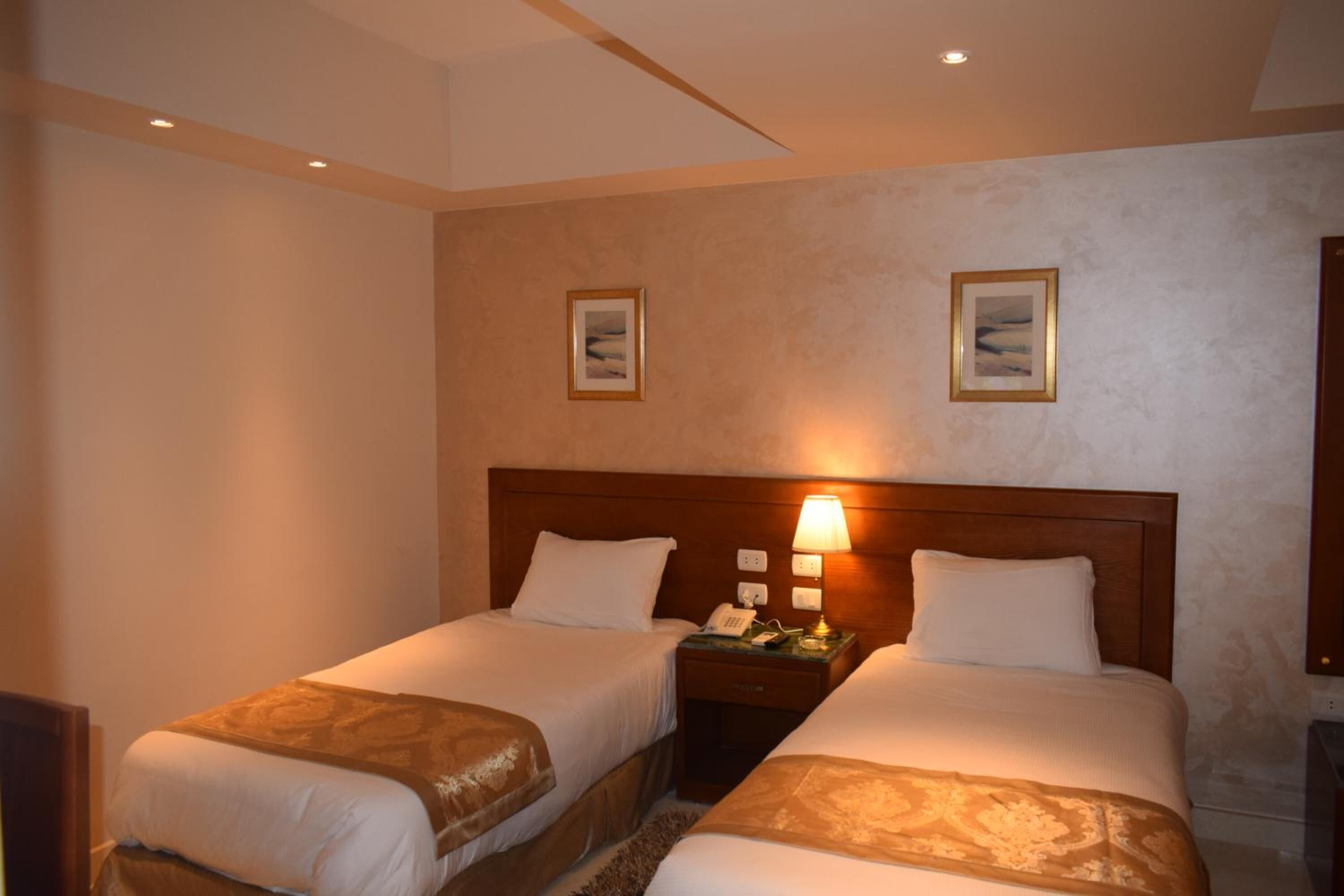 A hotel room with two beds, a nightstand with a lamp, and two framed pictures on the wall.