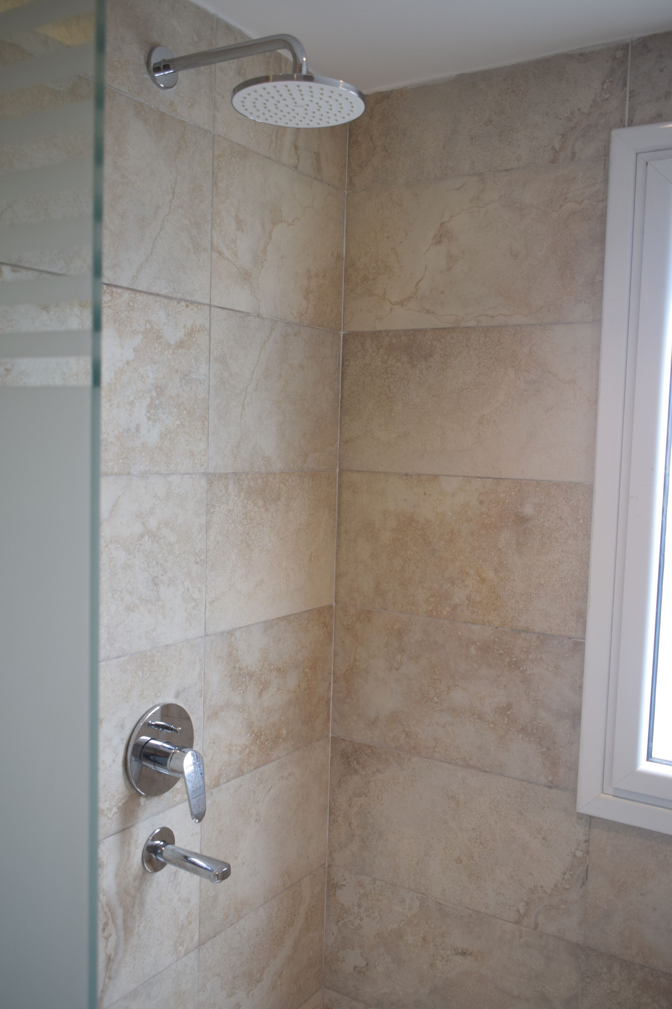 Une douche avec une porte en verre, un pommeau de douche à main et un panneau de commande fixé au mur.