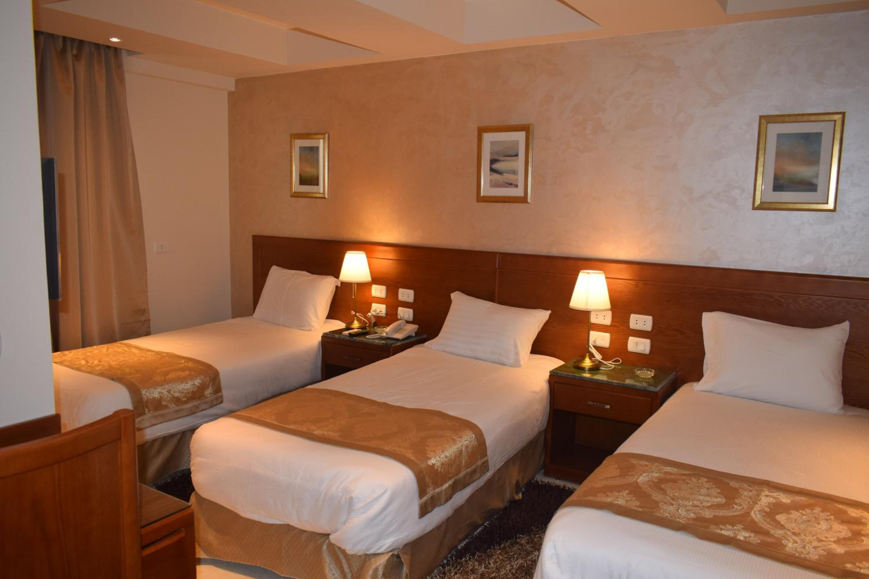 A hotel room with three single beds, each with a wooden headboard, bedside tables, and lamps.