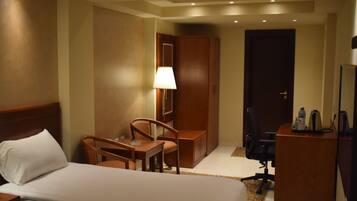 A hotel room with a bed, a desk, a chair, a lamp, and a wardrobe.