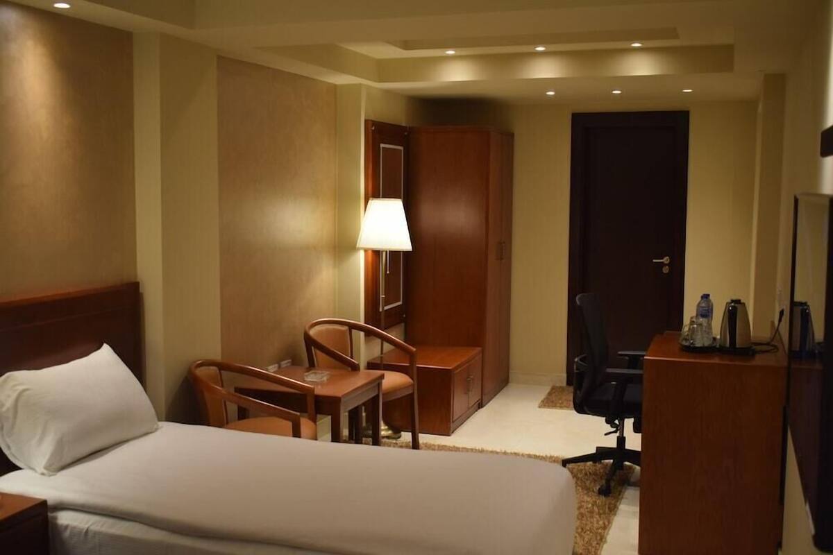 A hotel room with a bed, a desk, a chair, a lamp, and a wardrobe.