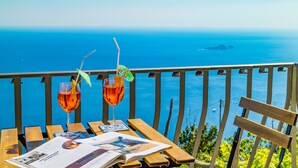 A wooden table with two glasses of red beverage, a menu, and a view of the sea. - Estate4home - GOAT PATH (Positano)