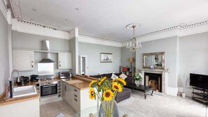 Una cocina moderna con una isla central, un área de comedor con mesa de vidrio y una sala de estar con chimenea.