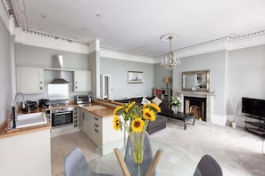 A modern kitchen with a central island, a dining area with a glass table, and a living room with a fireplace.