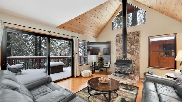 A spacious living room with a fireplace, leather sofas, and large windows offering a view of a snowy deck. - Exquisite Vacation Home with Hot Tub, EV Charger (Arnold)