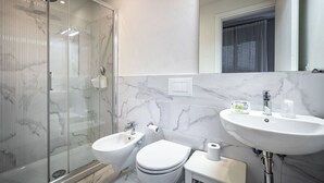A modern bathroom with a glass shower enclosure, a bidet, a toilet, and a sink with a mirror above.