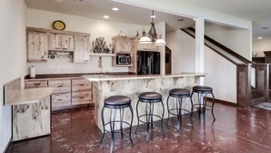 A modern kitchen with wooden cabinets, a central island with bar stools, a microwave, and a refrigerator.