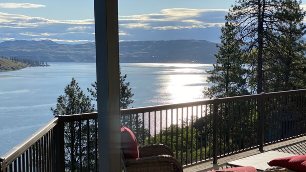 A deck with wicker furniture and a view of a lake and mountains.