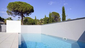 Ein Swimmingpool mit klarem, blauem Wasser, umgeben von einer weißen Mauer und einer gefliesten Liegefläche.