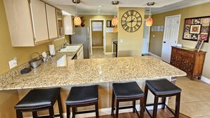 A kitchen with a large granite island, three bar stools, wooden cabinets, a refrigerator, and pendant lighting. - Luxury Getaway Branson Suite at the Greens at Thousand Hills! Great Rates!  (Branson)