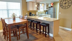 A modern kitchen with a central island, bar stools, wooden chairs, and a large wall clock. - Luxury Getaway Branson Suite at the Greens at Thousand Hills! Great Rates!  (Branson)