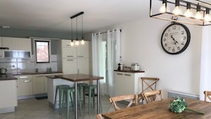 A modern kitchen with a dining area, featuring a wooden table and chairs, a clock, and a kitchen island with stools.