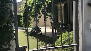 A gated entrance with a wrought iron gate, a well-maintained lawn, and a building with a tiled roof in the background.
