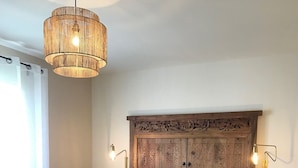 A bedroom with a large bed, two bedside tables, a wooden headboard with carvings, and a hanging light fixture.