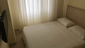 A neatly made bed with white linens in a room with a plain white wall and a window with sheer curtains. - Elmas Motel (Marmara)