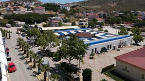 A large building with a blue and white roof, surrounded by palm trees and a parking lot. - Elmas Motel (Marmara)