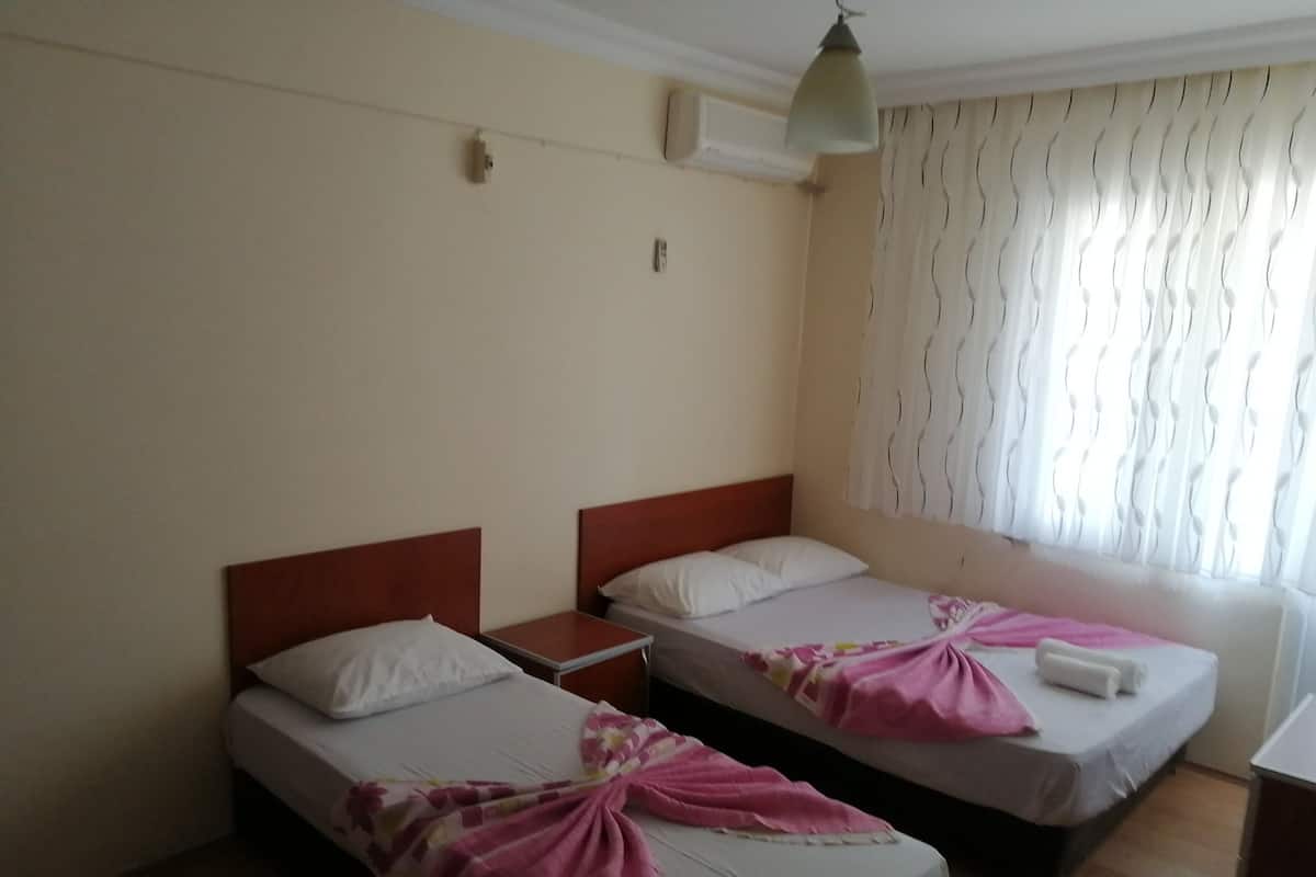 A hotel room with two single beds, a bedside table, a hanging lamp, and a window with curtains.