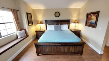 A bedroom with a large bed, two bedside tables with lamps, a window with curtains, and a picture on the wall.
