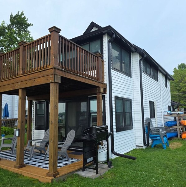 A two-story house with a wooden deck, outdoor seating, and a grill. - Lakefront Cottage on Portage Lake and the Huron River Chain of Lakes (Pinckney)