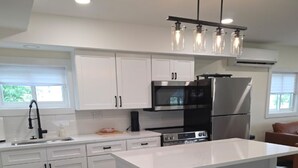 A modern kitchen with white cabinets, a central island with bar stools, a black refrigerator, and a stainless steel oven. - Lakefront Cottage on Portage Lake and the Huron River Chain of Lakes (Pinckney)