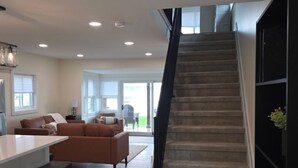 A modern interior with a staircase leading to an upper level, a kitchen area with a dining table, and a living space with sofas. - Lakefront Cottage on Portage Lake and the Huron River Chain of Lakes (Pinckney)