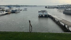 A marina with several boats docked, a grassy foreground, and a distant shoreline. - Lakefront Cottage on Portage Lake and the Huron River Chain of Lakes (Pinckney)