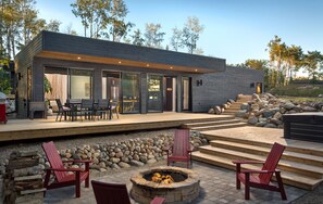 Ein modernes Haus mit Terrasse, Sitzgelegenheiten im Freien und einer Feuerstelle.