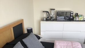 A neatly made bed with black and pink bedding, a bedside table with a lamp, and a white dresser with a coffee maker and other items. - Clean & Comfortable room near beaches, Eden, Heligan and Charlestown (St Austell)