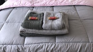 A neatly made bed with a pink and grey duvet, two grey pillows, and a pair of folded towels with a red logo on a hotel room. - Clean & Comfortable room near beaches, Eden, Heligan and Charlestown (St Austell)