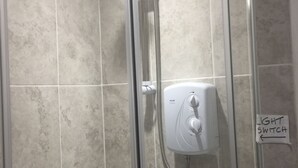 A glass-enclosed shower with a handheld showerhead, a wall-mounted control panel, and a sign indicating the location of the light switch. - Clean & Comfortable room near beaches, Eden, Heligan and Charlestown (St Austell)