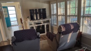 Una sala de estar con un sofá, dos sillones, un televisor y un aparador.