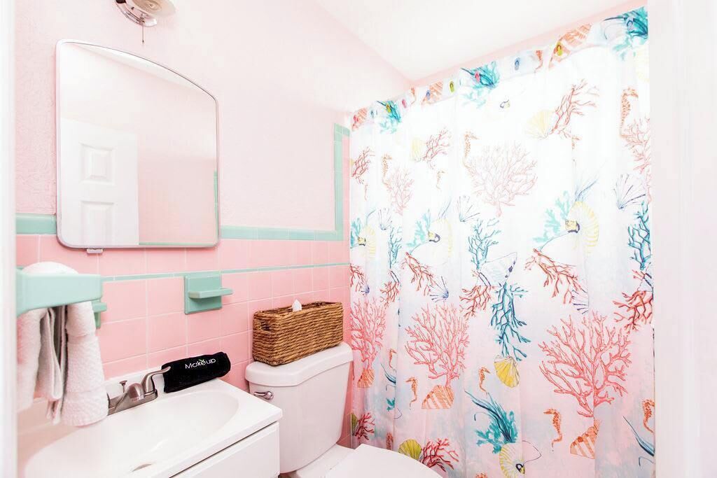 Un bagno con un lavandino bianco, uno specchio, un water e una tenda da doccia con motivo corallo.