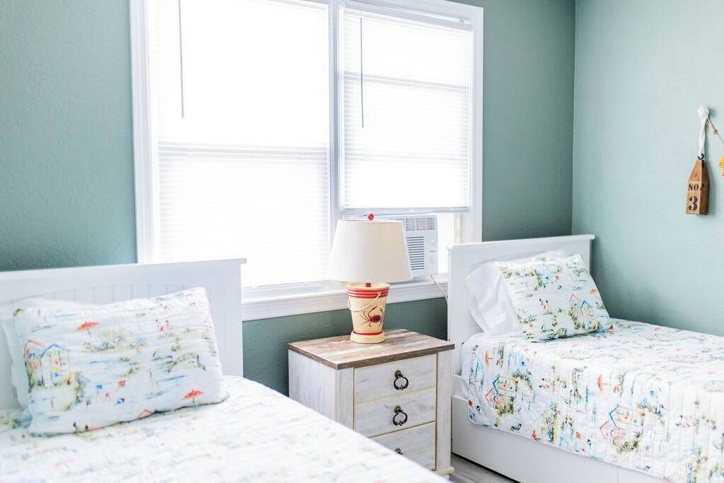 Une chambre avec deux lits, une table de chevet avec une lampe et une fenêtre avec des stores.