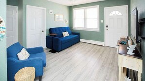 Ein Zimmer mit einem blauen Sofa, einer weißen Tür, einem Deckenventilator und einem Fenster.