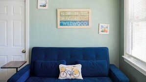 Ein blaues Sofa mit einem Kissen mit Fahrradmuster, einer gerahmten Karte mit Koordinaten und einem kleinen Bild an der Wand.