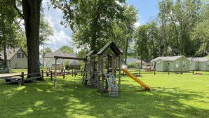 Un parque infantil con un tobogán y estructuras para escalar, rodeado de césped y árboles.