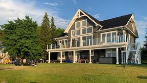 A large, two-story house with a covered porch and a stone retaining wall in the foreground. - Rare Waterfront Gem In Blue Mountain/Collingwood! Less than 2hrs from Toronto! (The Blue Mountains)