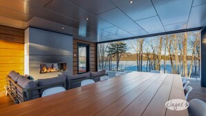 A modern interior with a large wooden table, a fireplace, and a view of a lake and trees. - 5 bdrm, 3 bath! Architectural gem! (Huntsville)
