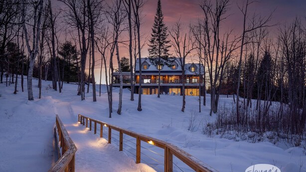 A snow-covered pathway leading to a lodge with a wooden railing, surrounded by trees. - 5 bdrm, 3 bath! Architectural gem! (Huntsville)