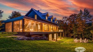 A modern house with large glass windows, a covered outdoor area, and a well-maintained lawn. - 5 bdrm, 3 bath! Architectural gem! (Huntsville)