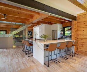 A modern kitchen with a central island, bar stools, and a view of the outdoors.